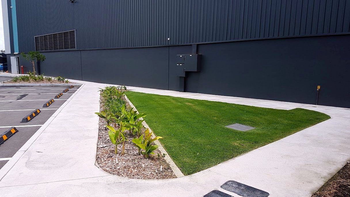 Mown lawn and planted beds along a large industrial warehouse